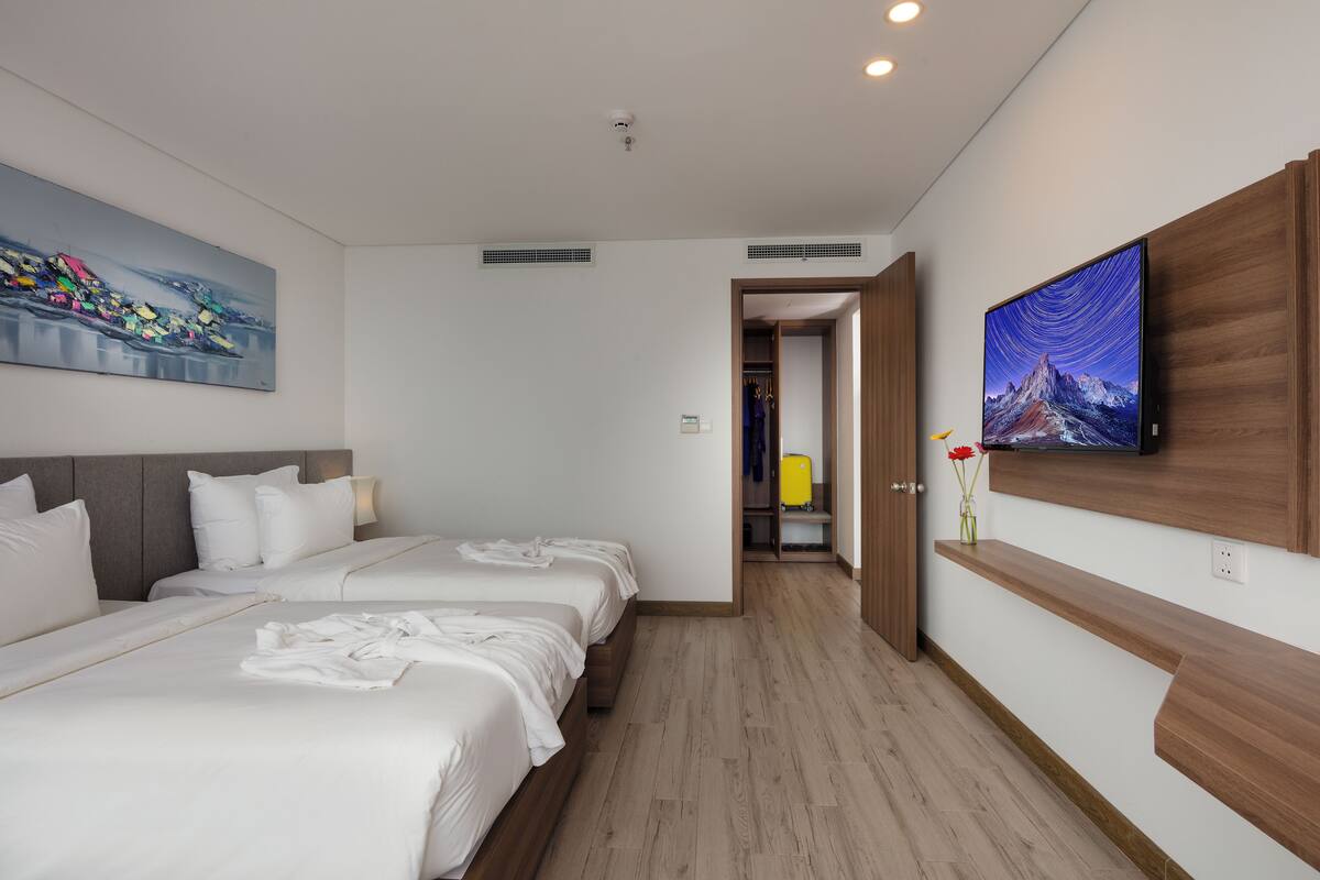 A hotel room with two beds, a large painting on the wall, a television, and a wooden shelf.