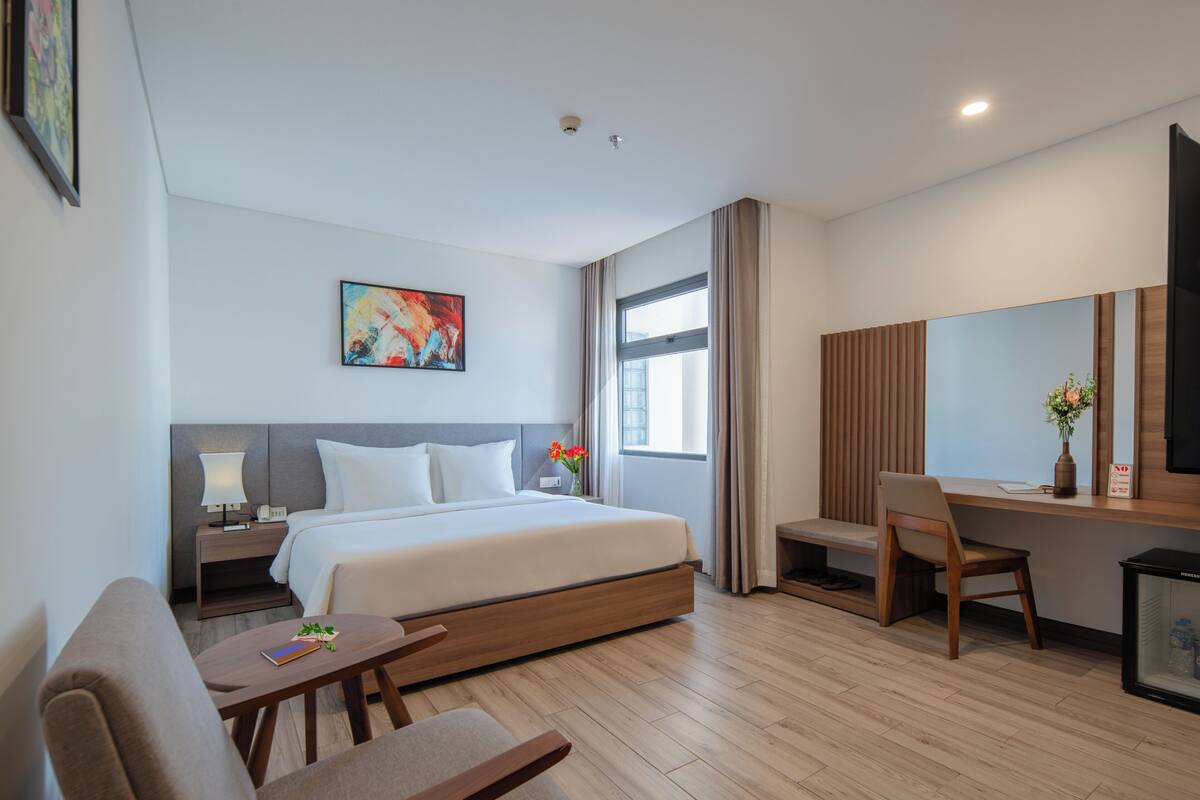 A modern hotel room with a bed, a desk, a chair, and a TV.
