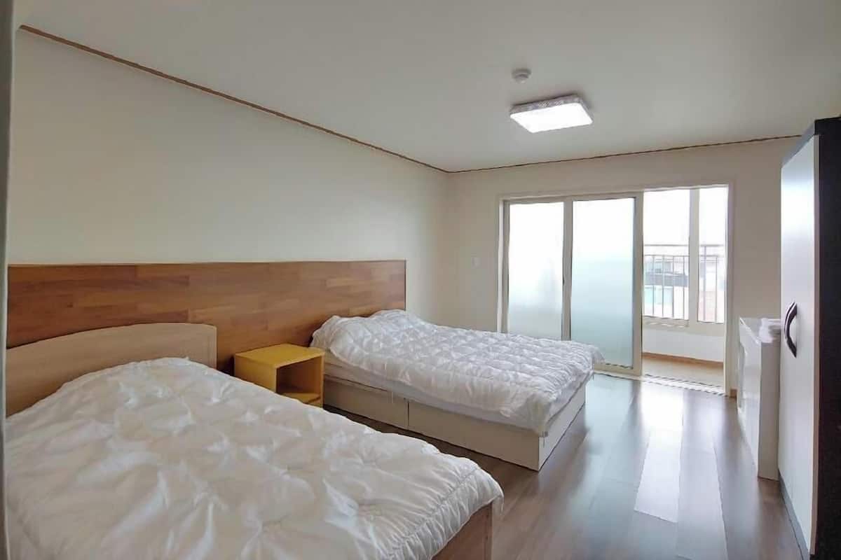 Una habitación de hotel moderna con dos camas, un cabecero de madera, una mesita de noche pequeña y un amplio ventanal corredero que da a un balcón.