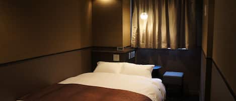 A hotel room with a bed, a nightstand, a small table, and a window with curtains.