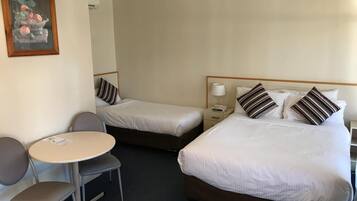 A hotel room with two single beds, a small round table with a chair, and a painting on the wall.