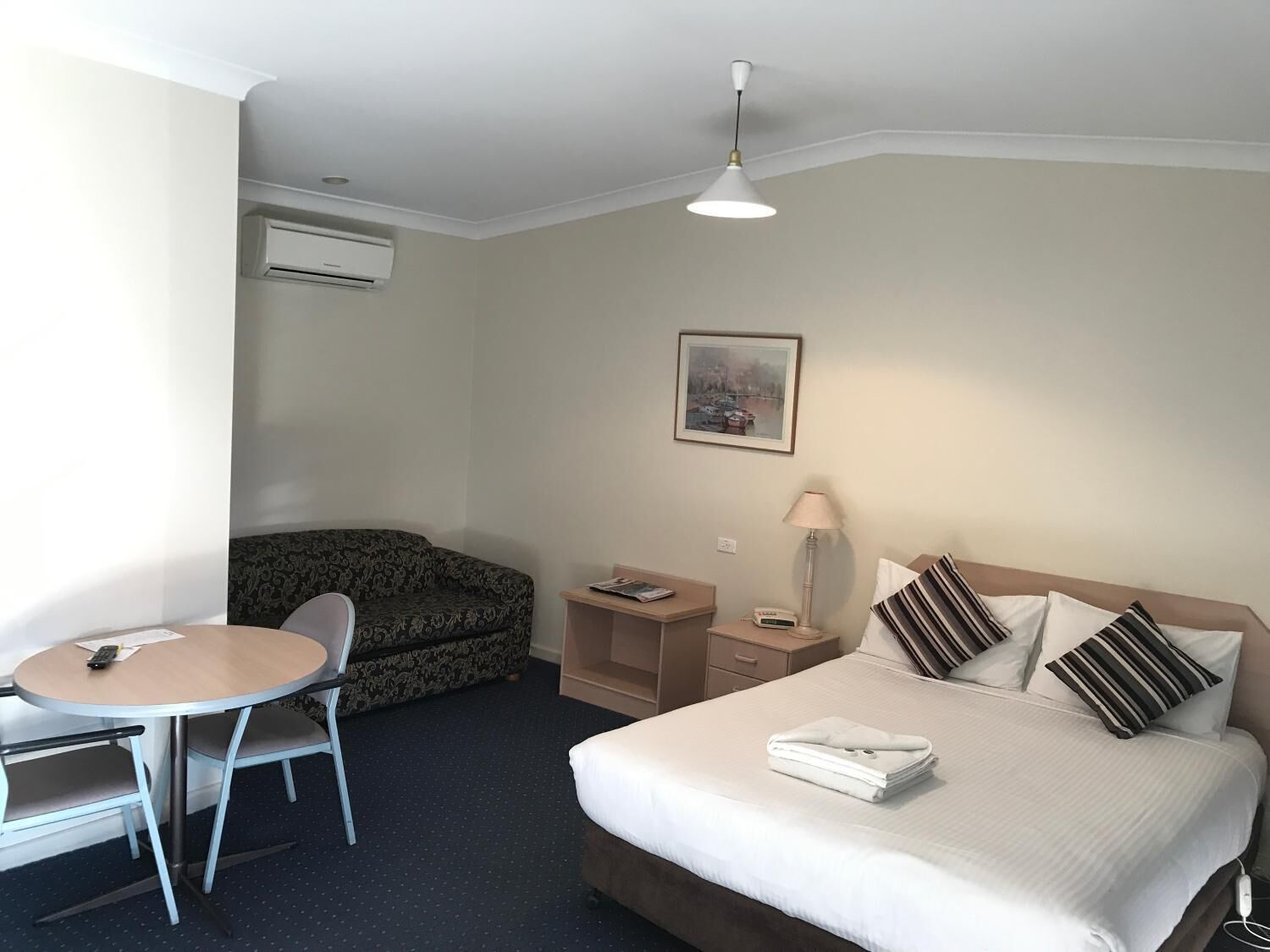 A hotel room with a bed, a desk, a chair, a lamp, and a painting on the wall.