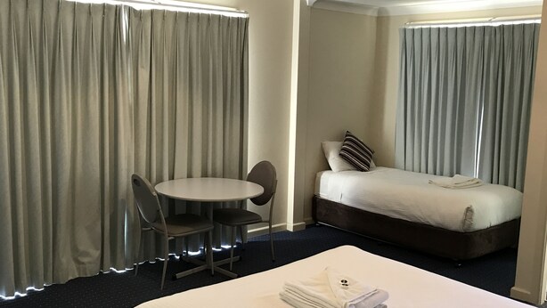 A hotel room with a bed, a small table with two chairs, and a window with curtains. - Orange Motor Lodge (Orange)
