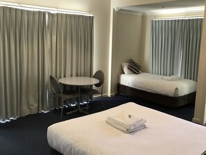 Une chambre d’hôtel avec un lit, une petite table et deux chaises, ainsi qu’une fenêtre avec des rideaux.