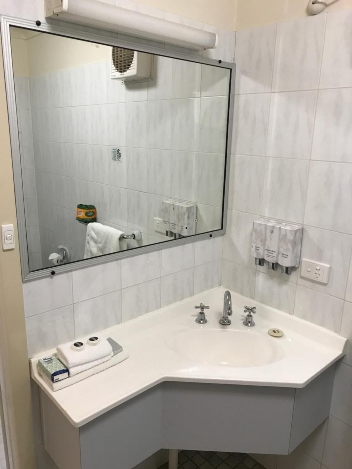 Une salle de bain avec un grand miroir, un lavabo blanc doté de deux robinets et un porte-serviettes avec une serviette.