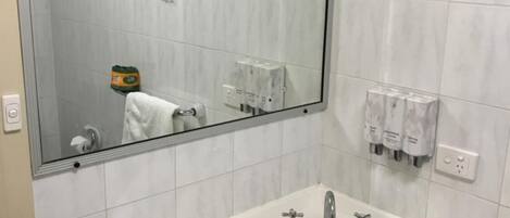 Un baño con un espejo grande, un lavabo blanco con dos grifos y un perchero con una toalla.