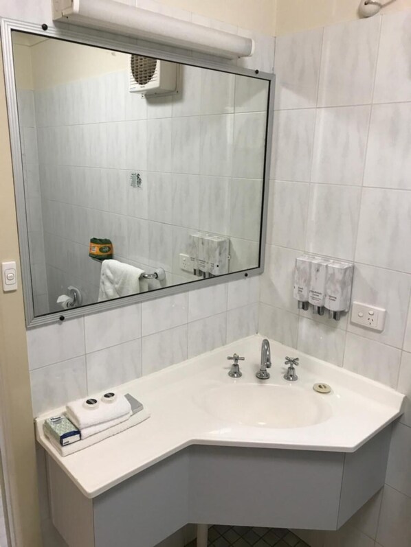 Un baño con un espejo grande, un lavabo blanco con dos grifos y un perchero con una toalla.