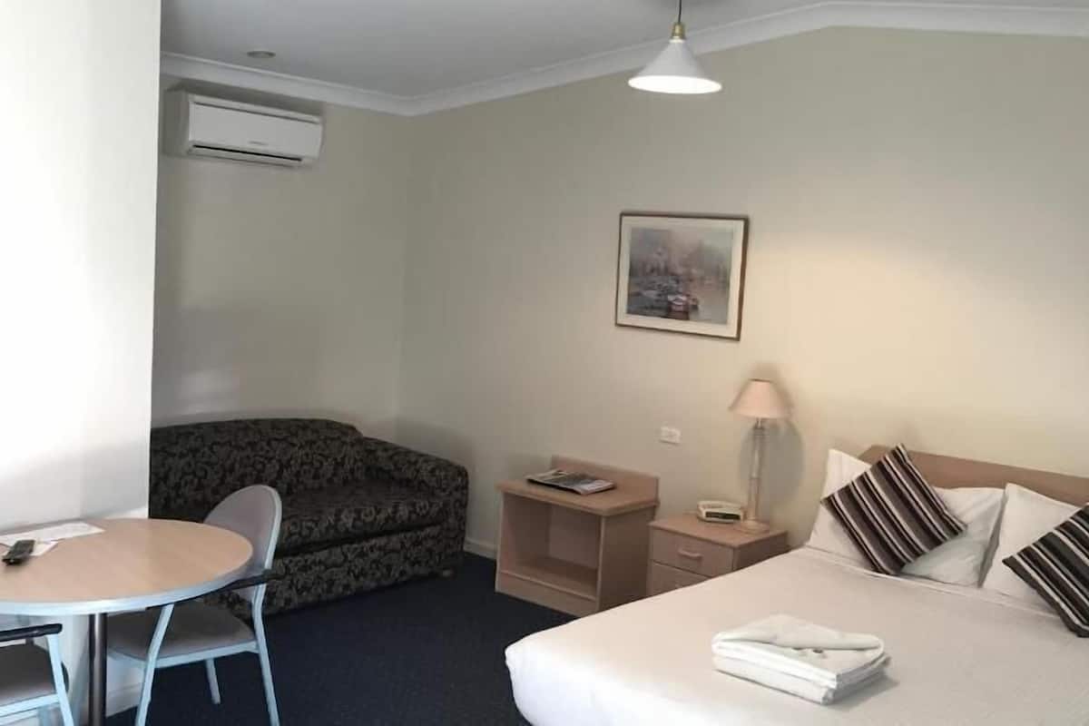 A hotel room with a bed, a desk, a chair, a sofa, a lamp, and a painting on the wall.