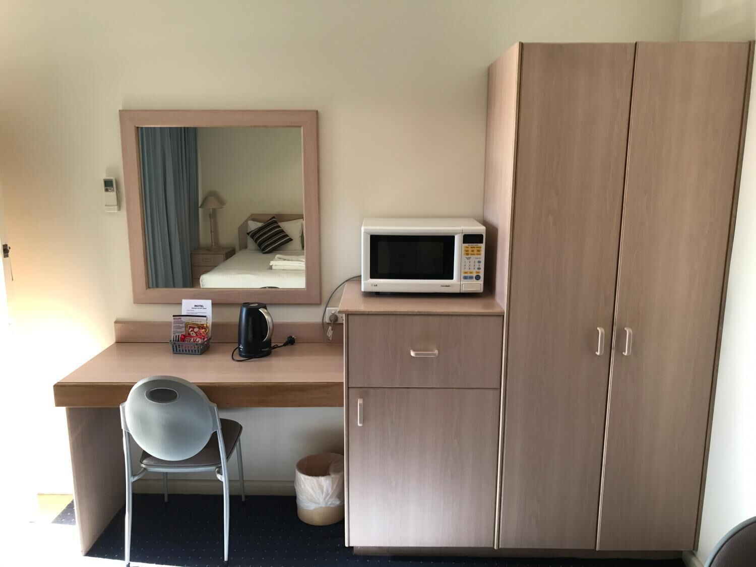 A compact hotel room with a wooden desk, a microwave, a chair, and a wardrobe.