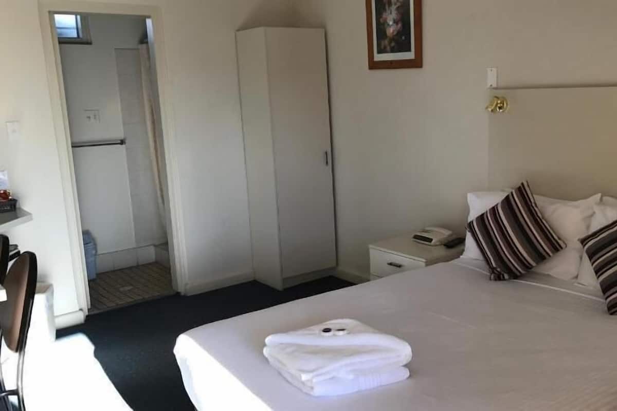 A hotel room with a bed, a bedside table, a wardrobe, and a door leading to a bathroom.