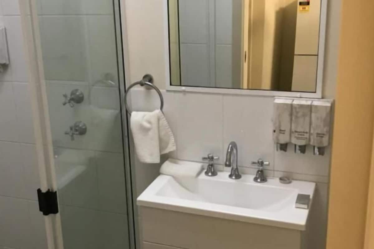 A bathroom with a glass shower enclosure, a sink with a mirror, and towel dispensers.