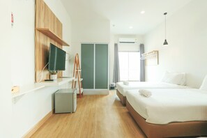 A modern hotel room with a wooden floor, a TV mounted on the wall, a desk with a lamp, a wardrobe, and a bed with white linens. - ALEXA Nimman - Hostel (Chiang Mai)