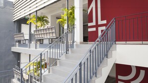 A modern building with a staircase, outdoor seating, and palm trees. - ALEXA Nimman - Hostel (Chiang Mai)