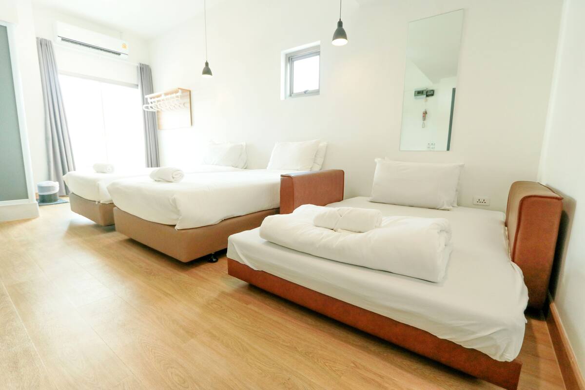 A hotel room with two beds, a window, and a mirror.