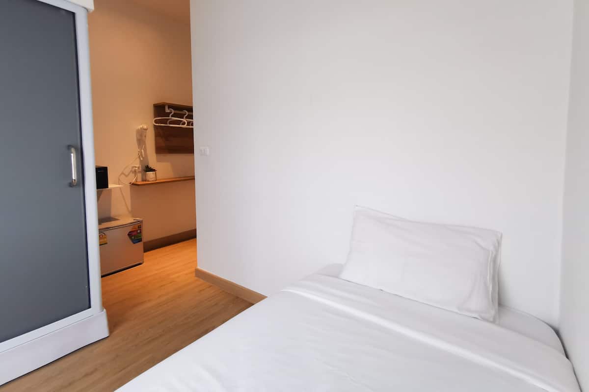 A bedroom with a bed, a door, and a small kitchenette area with a microwave and a plant.