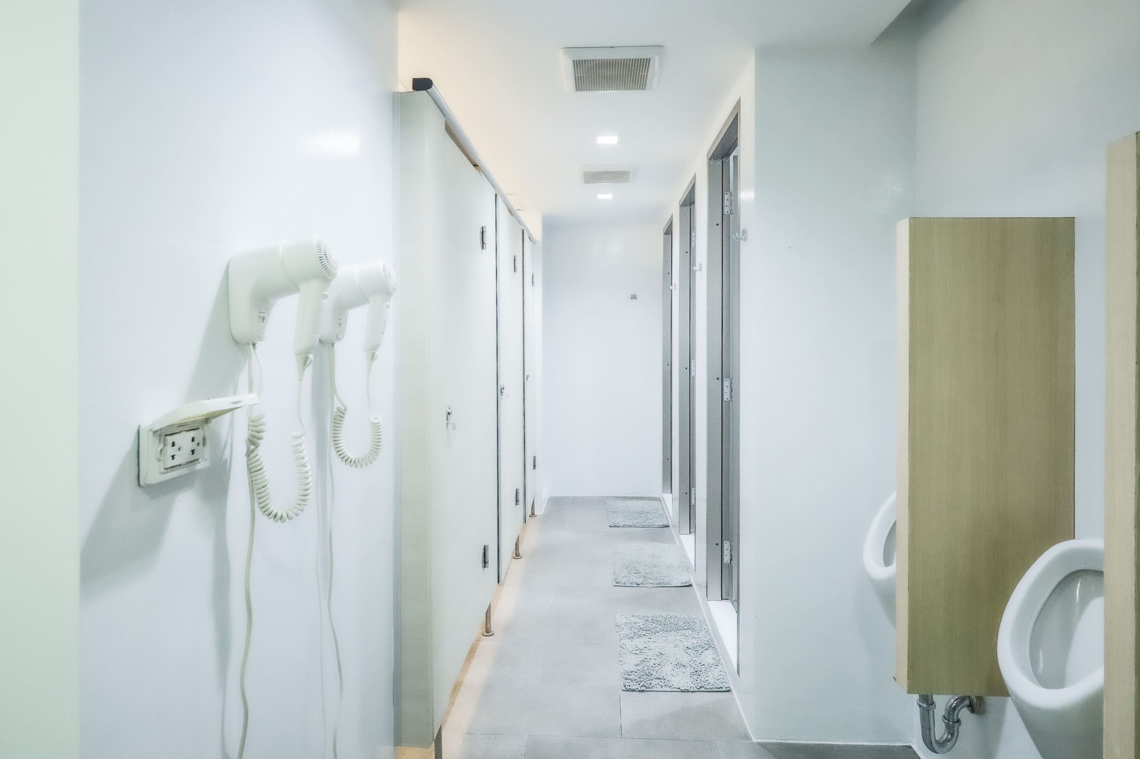 A modern bathroom with white walls, a wooden vanity, and a row of urinals.