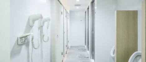 A modern bathroom with white walls, a wooden vanity, and a row of urinals.