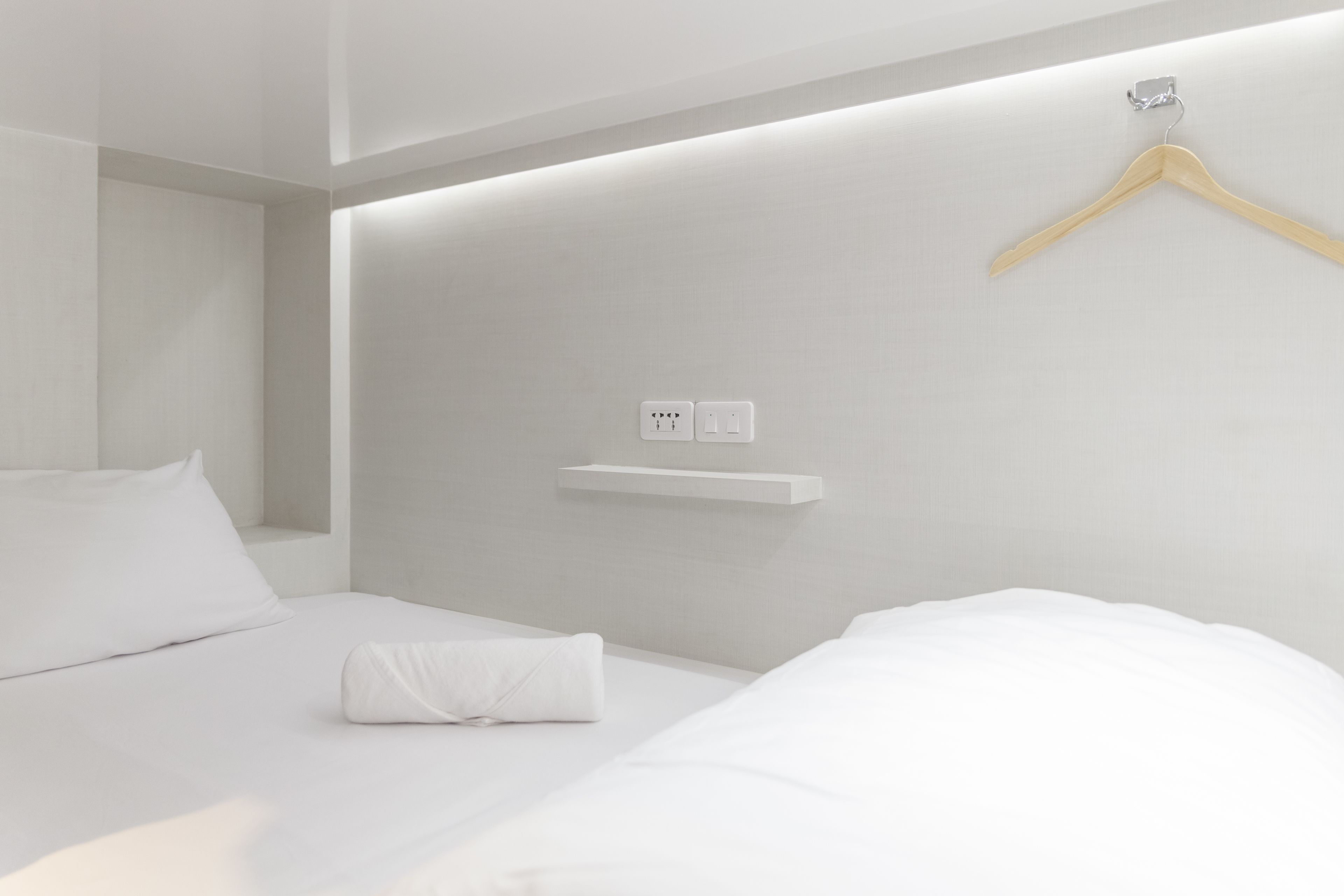Une chambre d’hôtel moderne avec un lit soigneusement fait, un cintre en bois accroché au mur et une petite étagère.