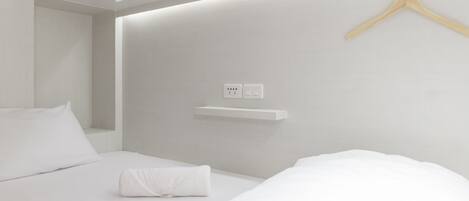 Une chambre d’hôtel moderne avec un lit soigneusement fait, un cintre en bois accroché au mur et une petite étagère.