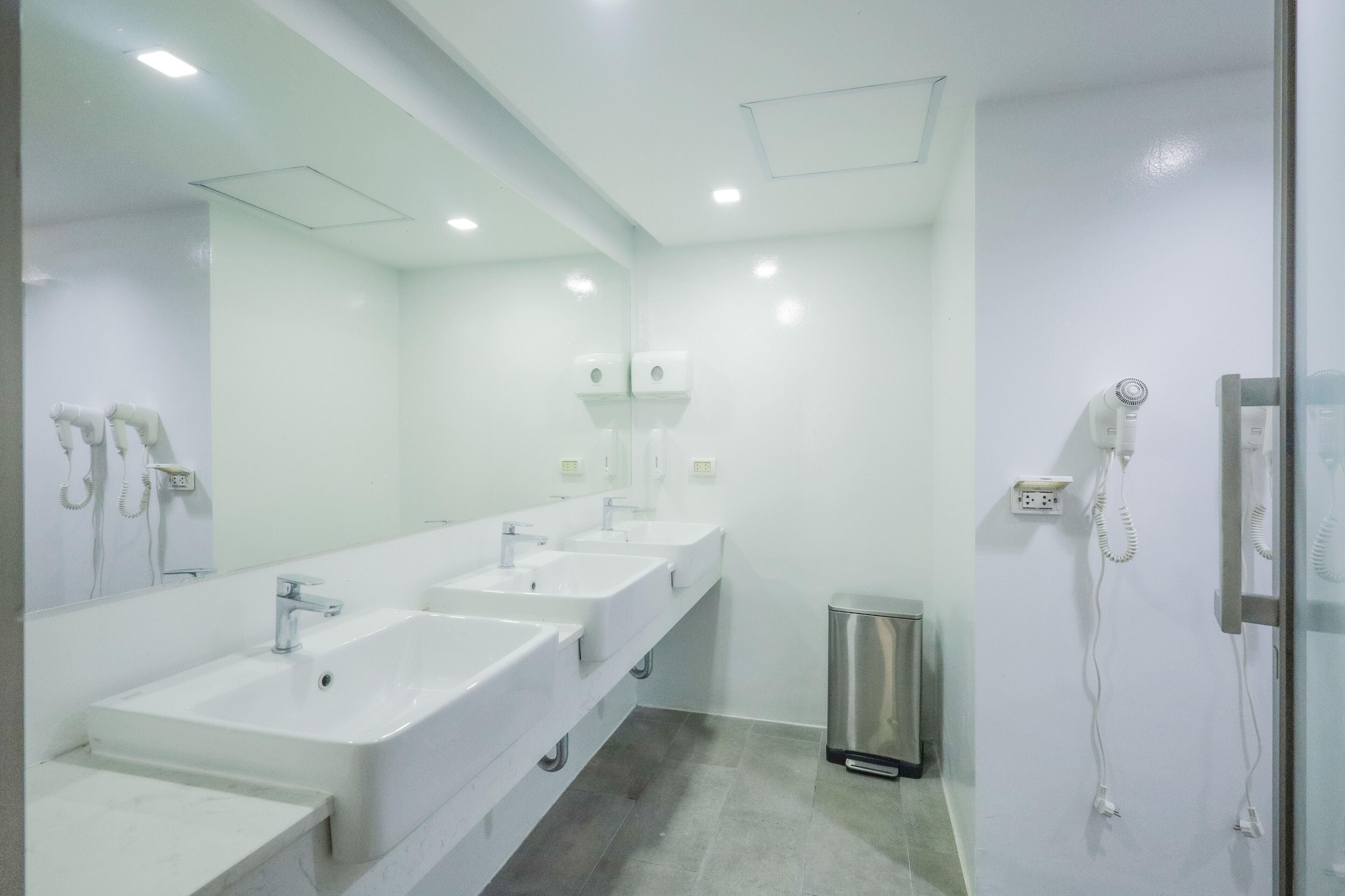 A modern bathroom with three sinks, a mirror, and a hairdryer.