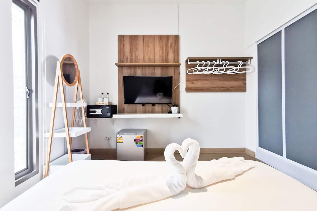 A modern bedroom with a bed, a TV, a shelf with toiletries, and a decorative sign.