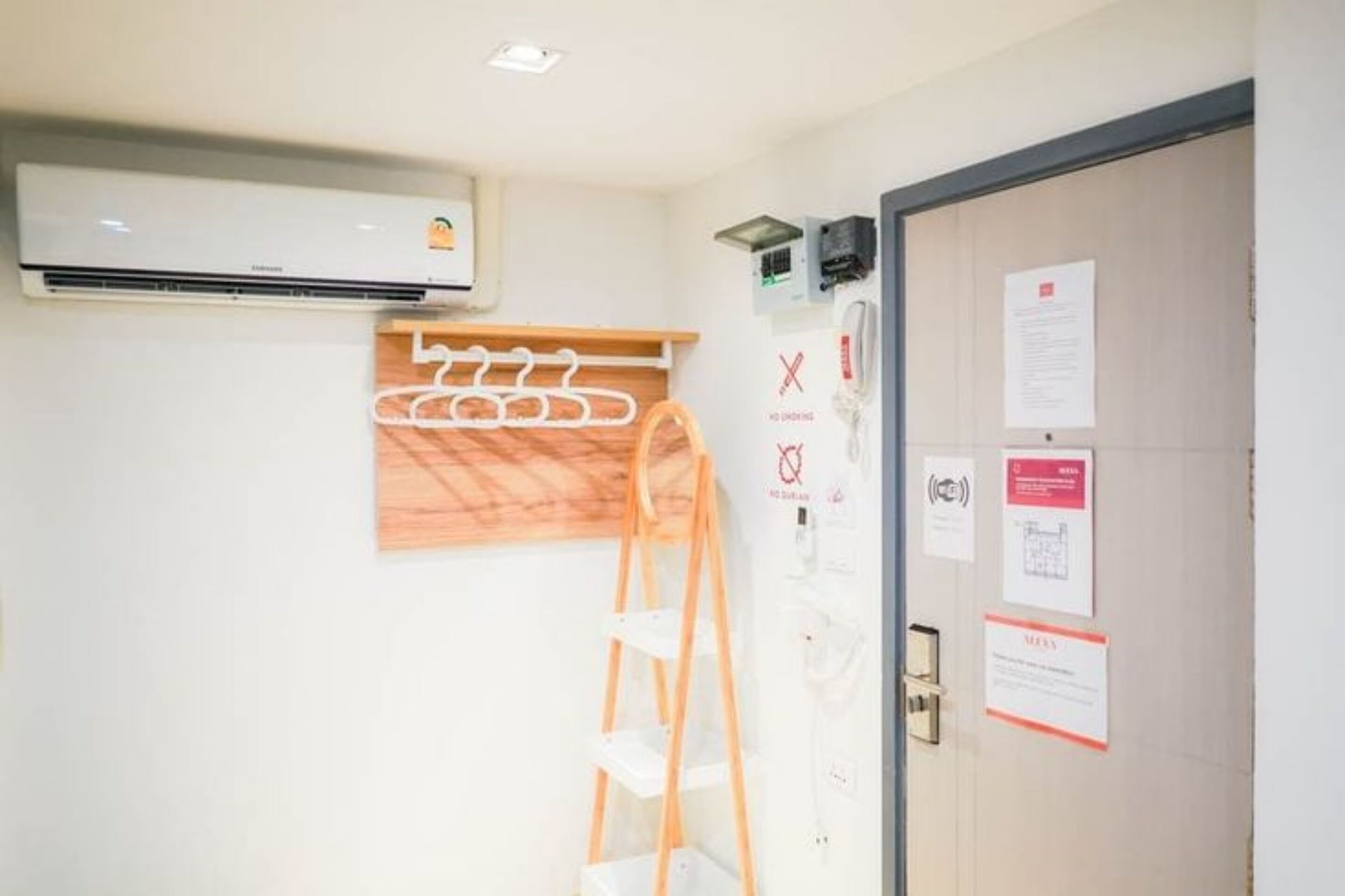 A hotel room with a wooden shelf, a white air conditioning unit, and a door with informational notices.