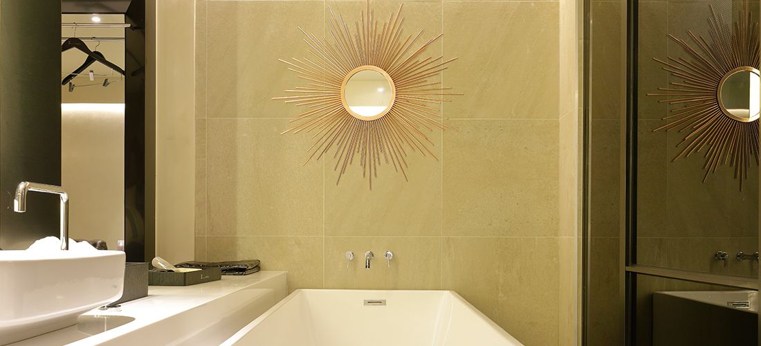 A modern bathroom with a freestanding bathtub, a wall-mounted vanity with a mirror, and a sunburst light fixture above the bathtub.