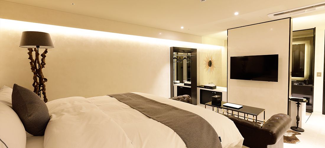 Una habitación de hotel moderna con una cama grande, mesitas de noche, un televisor y un espejo.