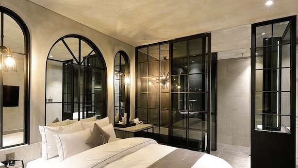 A modern bedroom with a large bed, a bedside table, a mirror, and a wall-mounted TV.