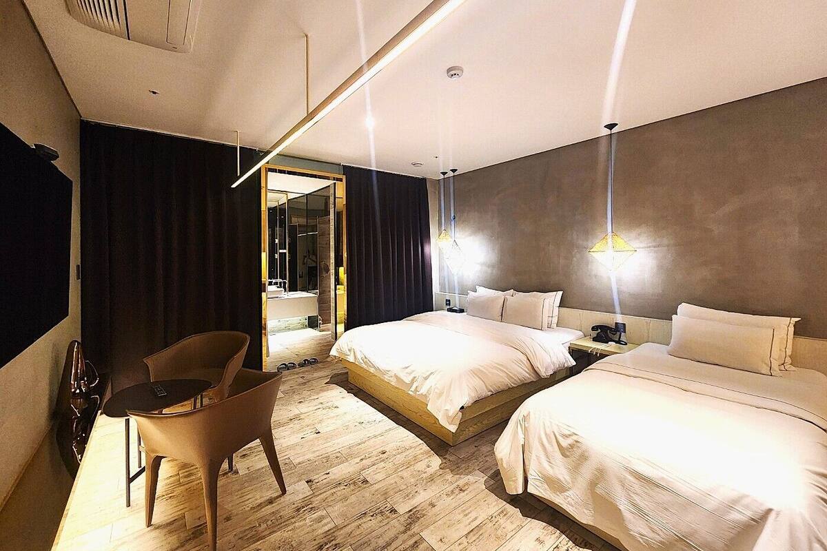 A modern hotel room with two beds, a desk, and a chair.