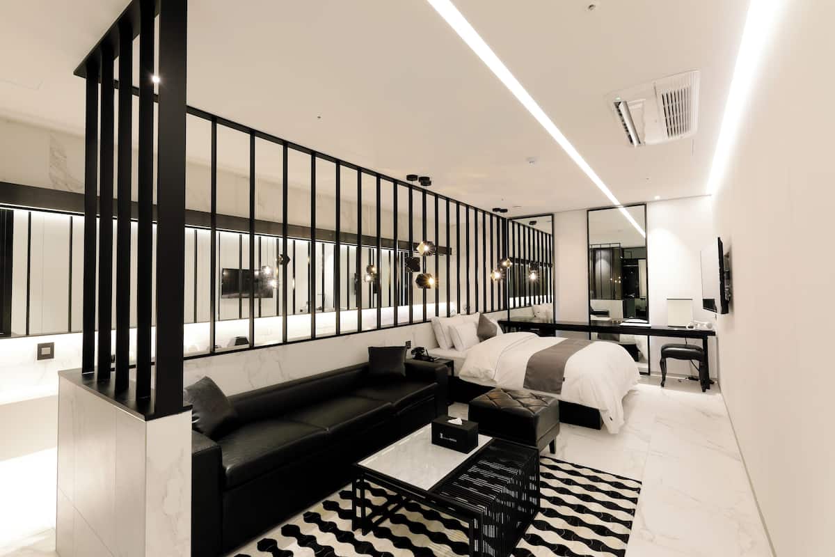 A modern bedroom with a black and white color scheme, featuring a sofa, a bed, a desk, and a large mirror.