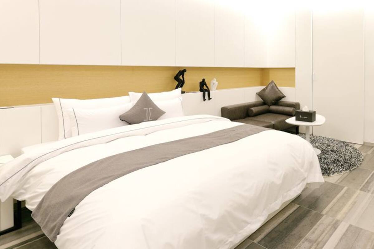 A modern bedroom with a large bed, a small sofa, a bedside table, and a TV.