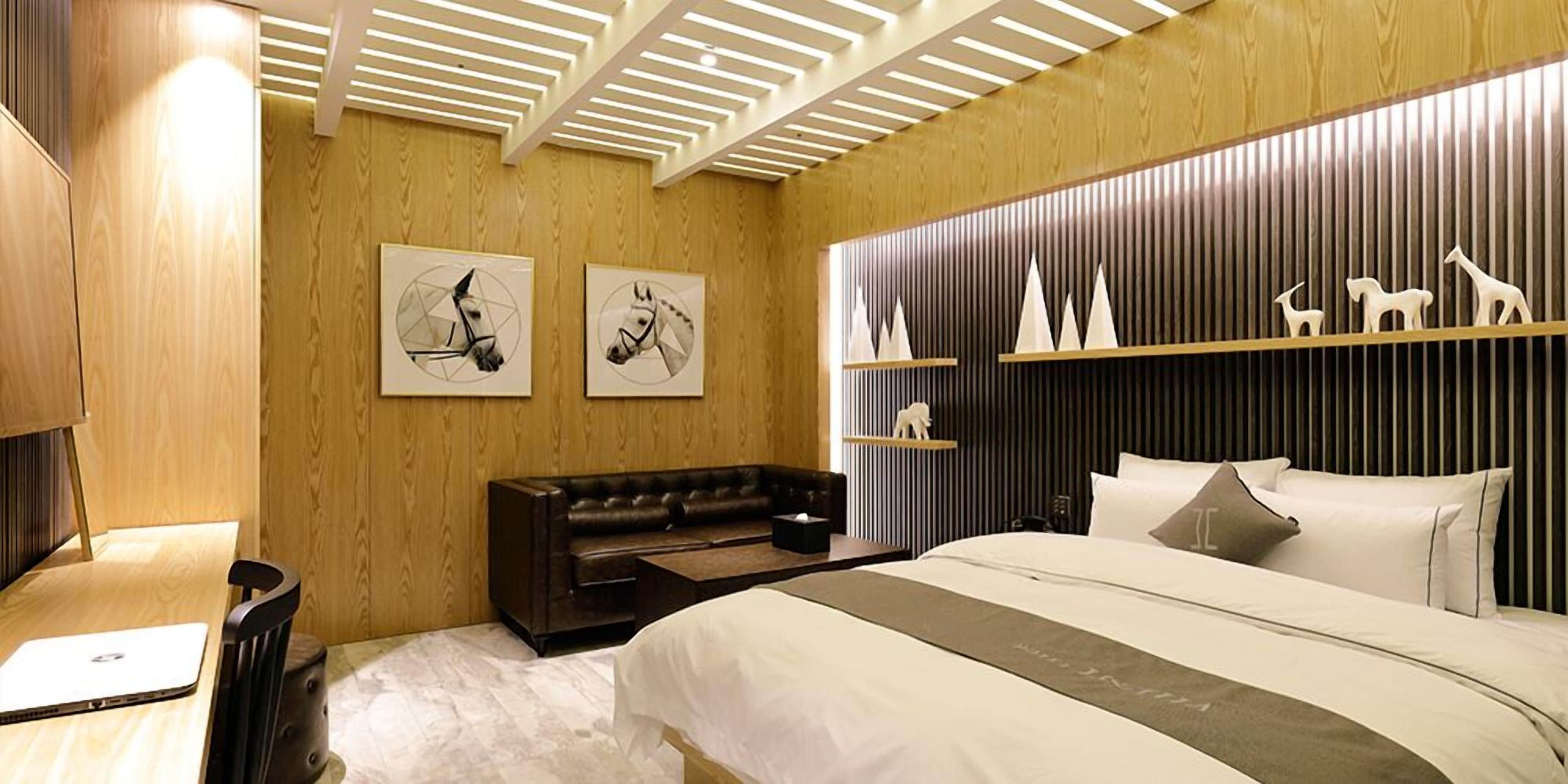 A modern bedroom with a wooden ceiling, a large bed with white bedding, a dark leather sofa, and wall-mounted shelves with decorative items.