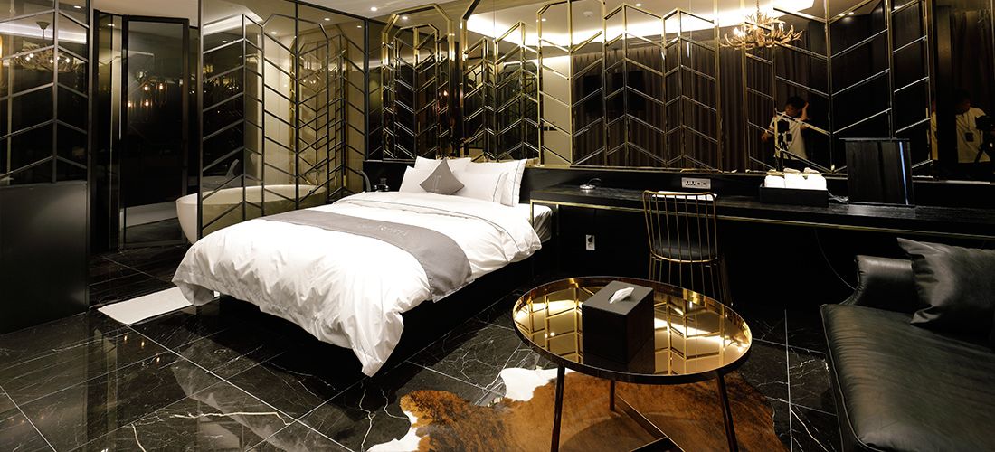 A modern hotel room with a large bed, a desk, a chair, and a round table.