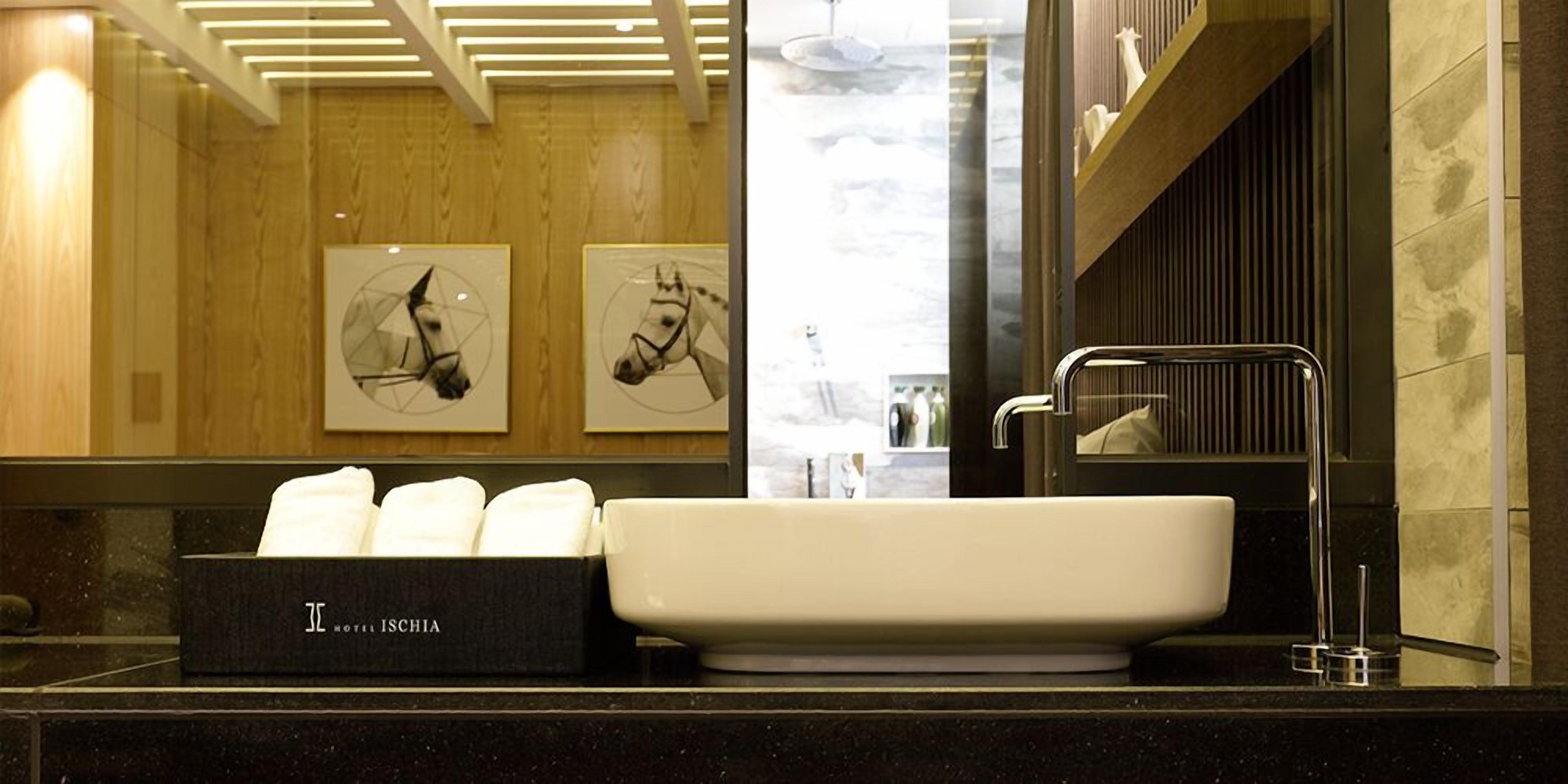 A hotel bathroom with a black countertop, a white sink, and a towel box labeled "HOTEL ISCHIA".