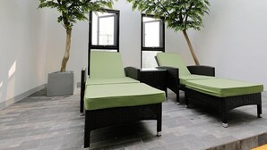 A room with two wicker lounge chairs with green cushions, a small table, and two potted plants.