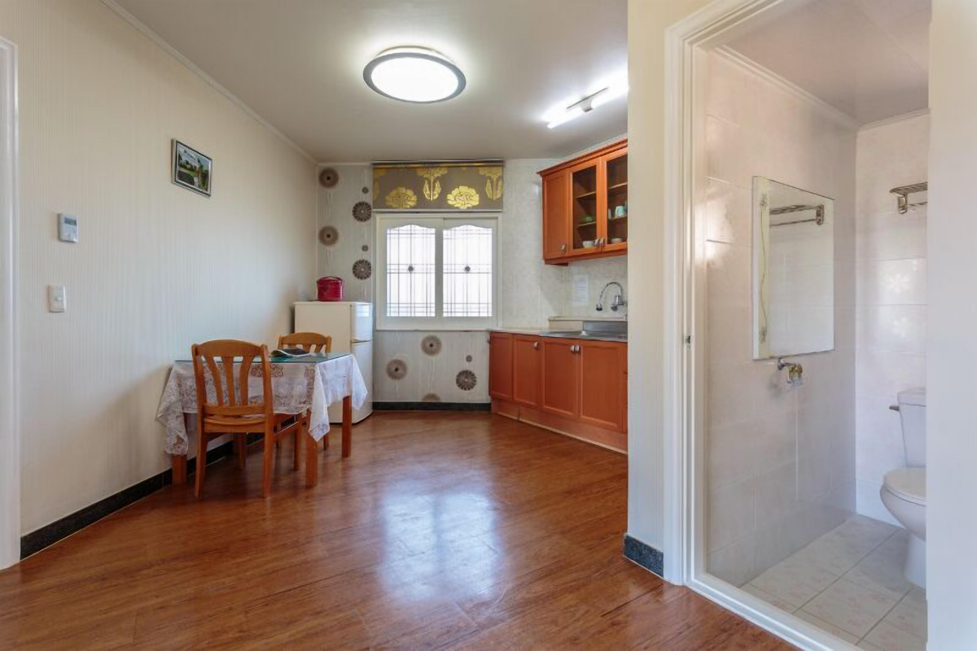A compact kitchen with wooden cabinets, a dining table with chairs, a window with decorative paper, and a shower area.