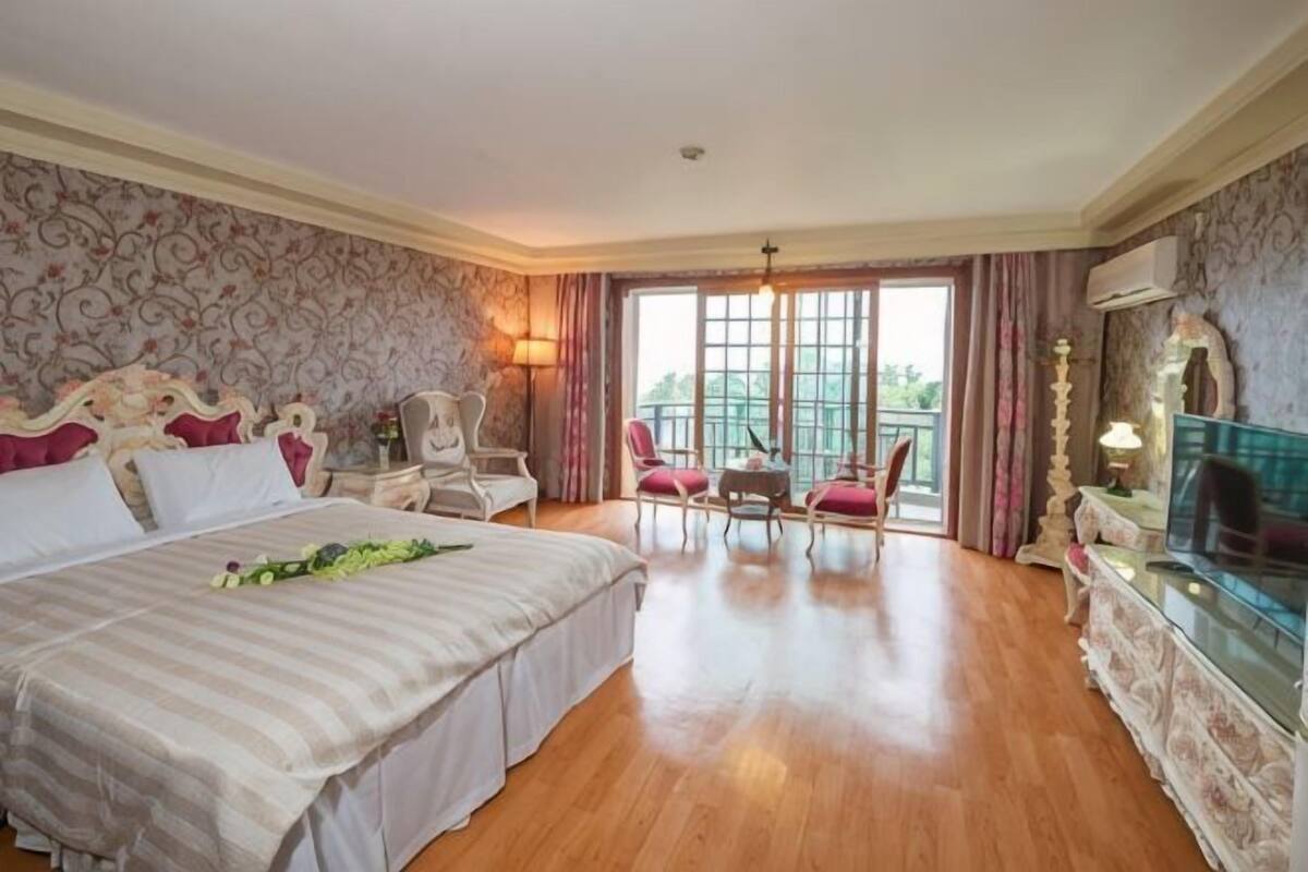 Hotelkamer met een groot bed, een bureau, een stoel, een televisie en een balkon met gordijnen.