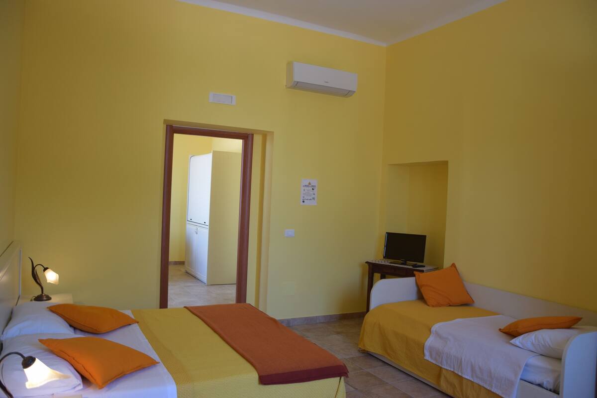 A room with two beds, a desk with a computer, and an air conditioning unit on the wall.