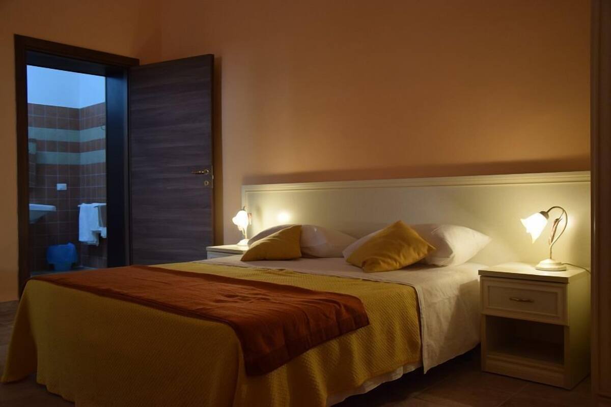 A hotel room with a bed, bedside tables, and a view of the outside.