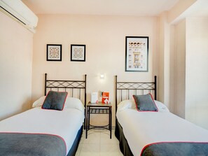 A hotel room with two beds, a small table, and a framed picture on the wall.