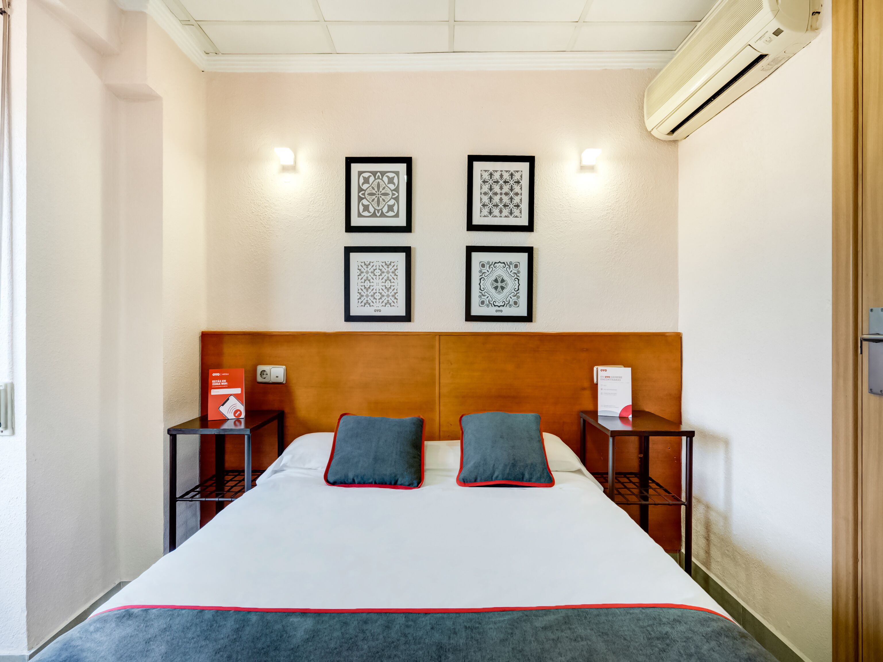 A hotel room with a large bed, two bedside tables, a headboard, and four framed pictures on the wall.