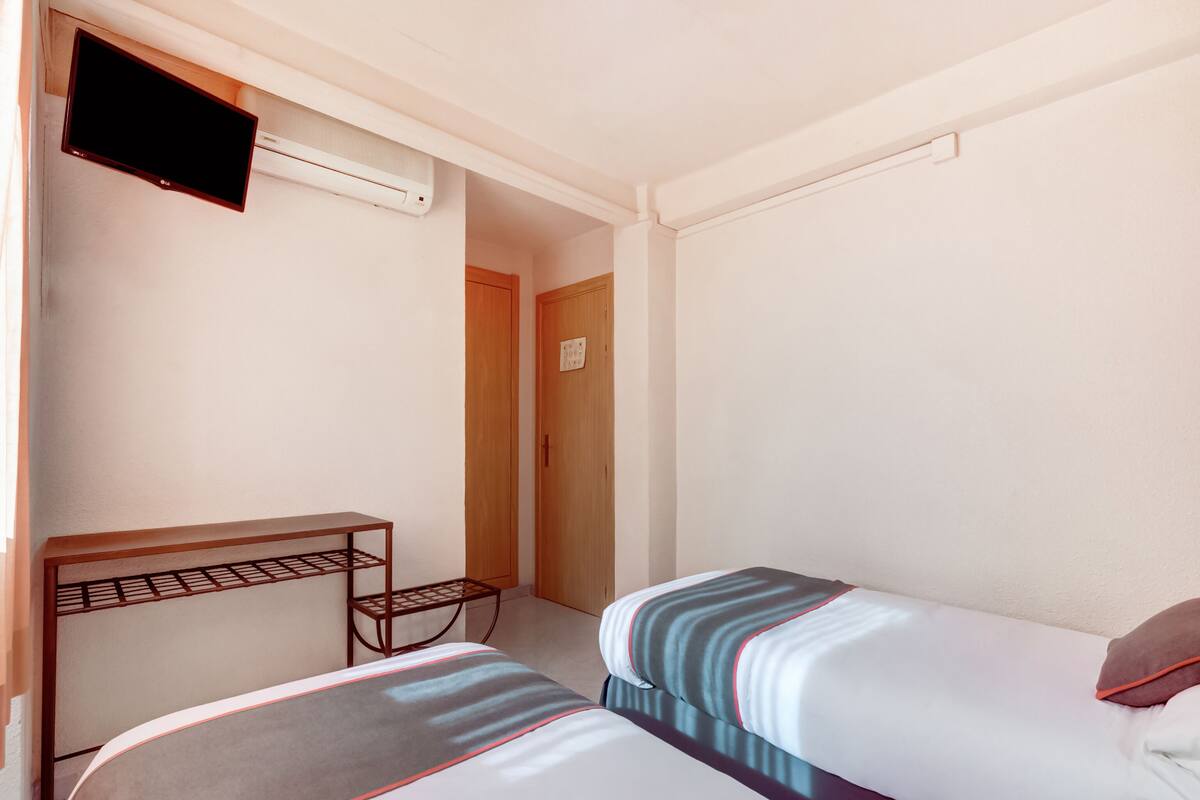 A hotel room with two beds, a small table, a TV, and an air conditioning unit.