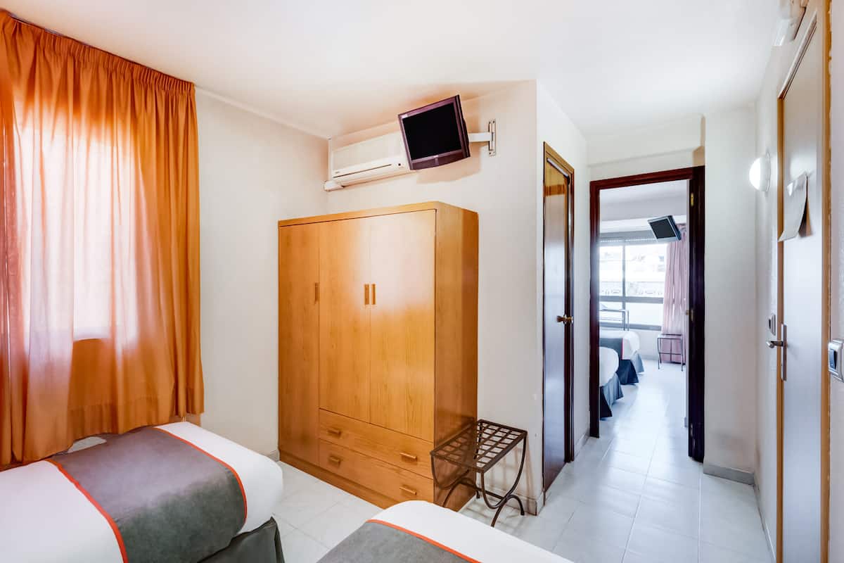 A hotel room with a wardrobe, a television, a bed, and a small table.