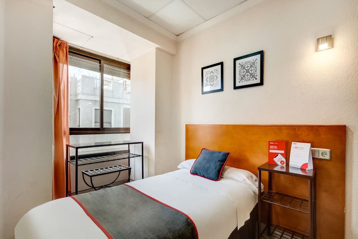 A hotel room with a bed, a nightstand, a window with curtains, and two framed pictures on the wall.