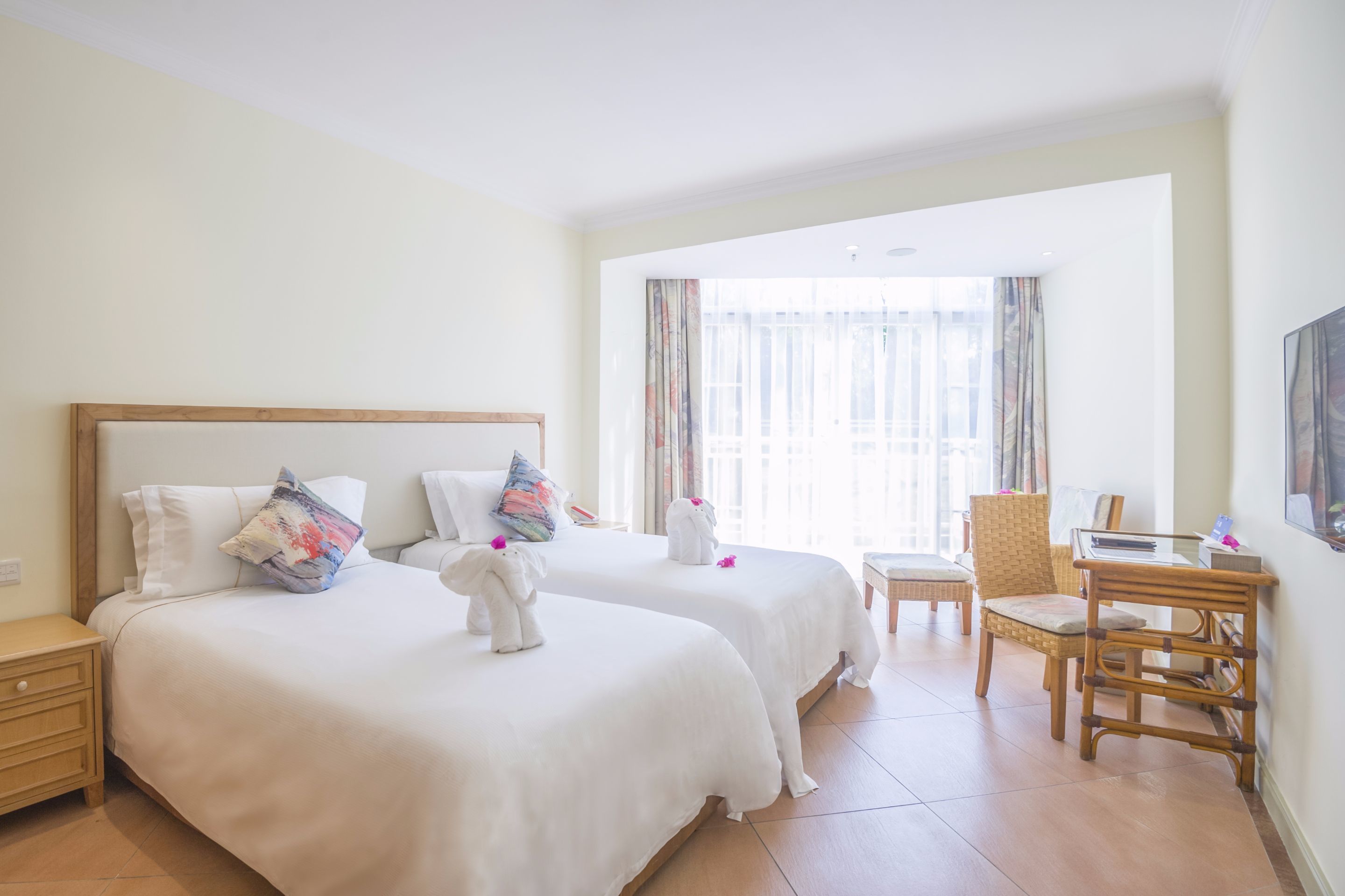 A hotel room with two beds, a desk, a chair, and a large window with curtains.