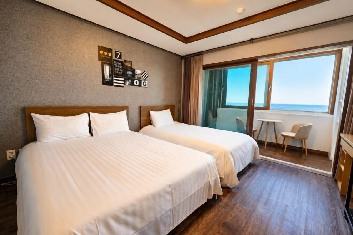 Une chambre d’hôtel avec deux lits, une petite table et vue sur la mer.