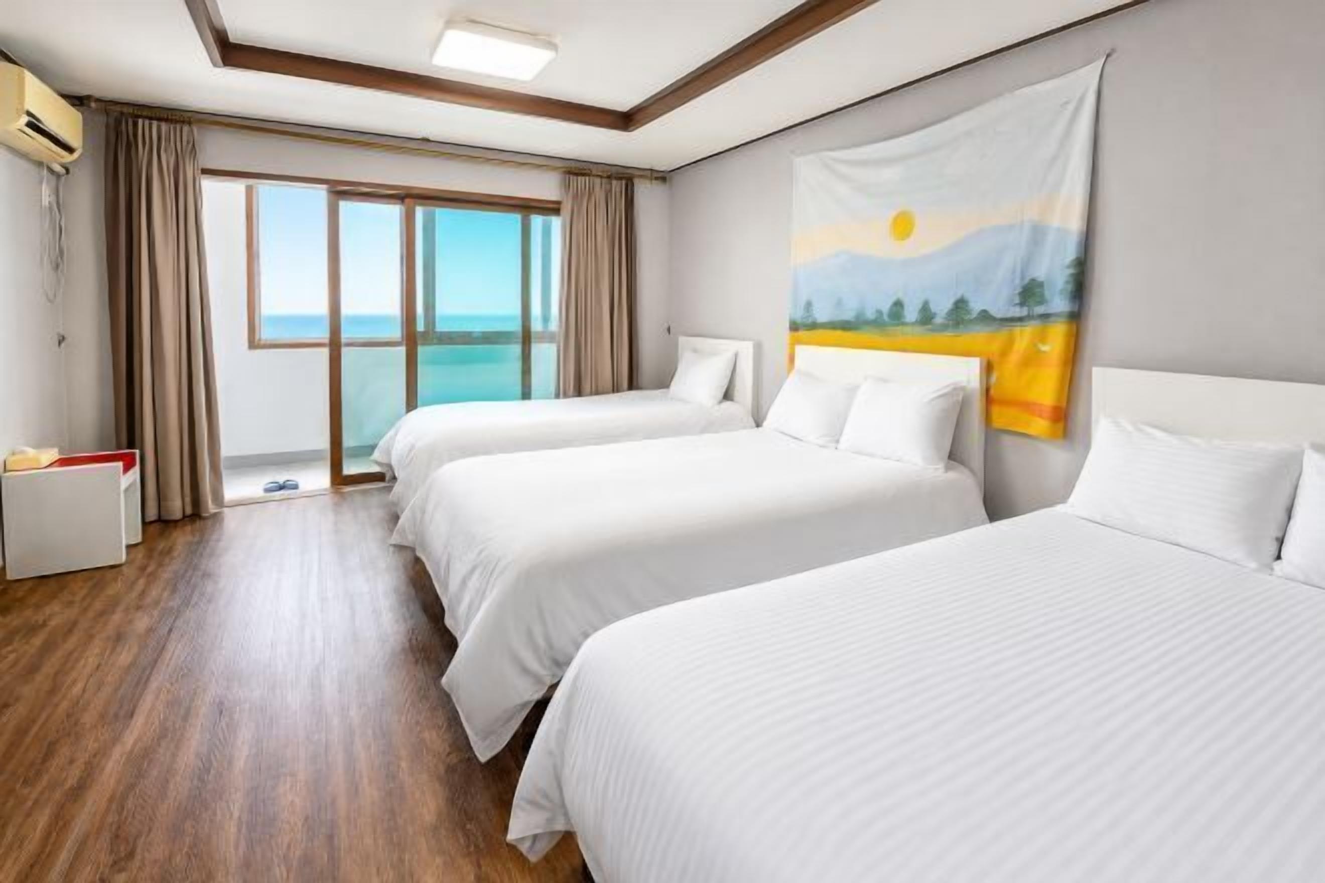 A hotel room with two beds, a large window, and a painting on the wall.
