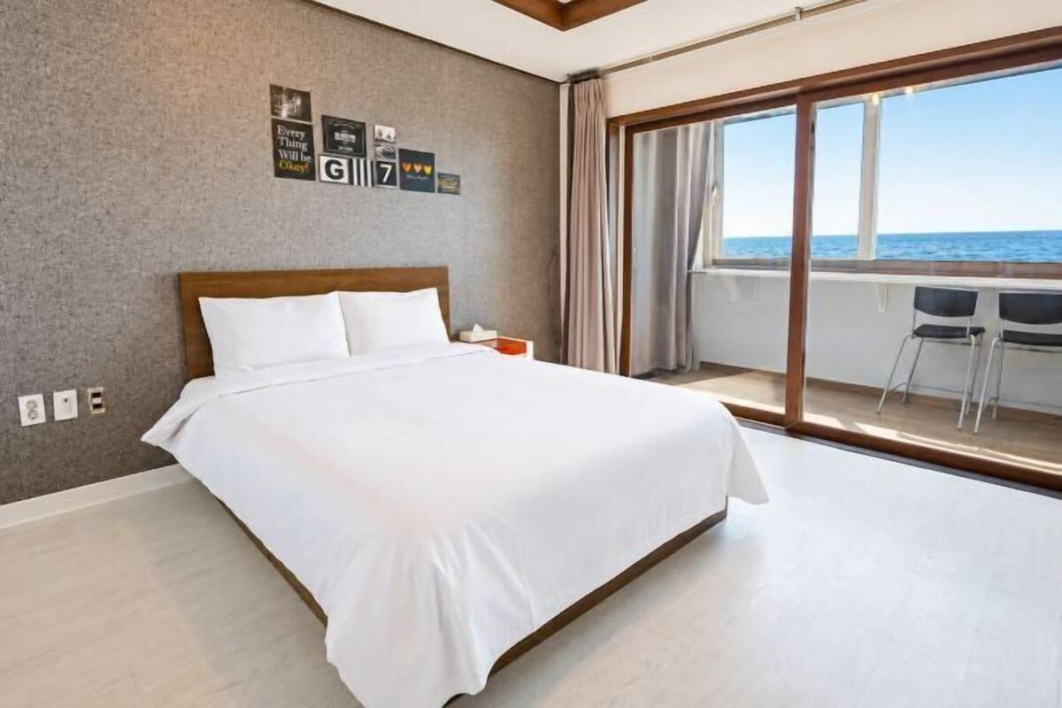 Une chambre d’hôtel avec un grand lit, une vue sur la mer depuis un balcon et un bureau avec des chaises.