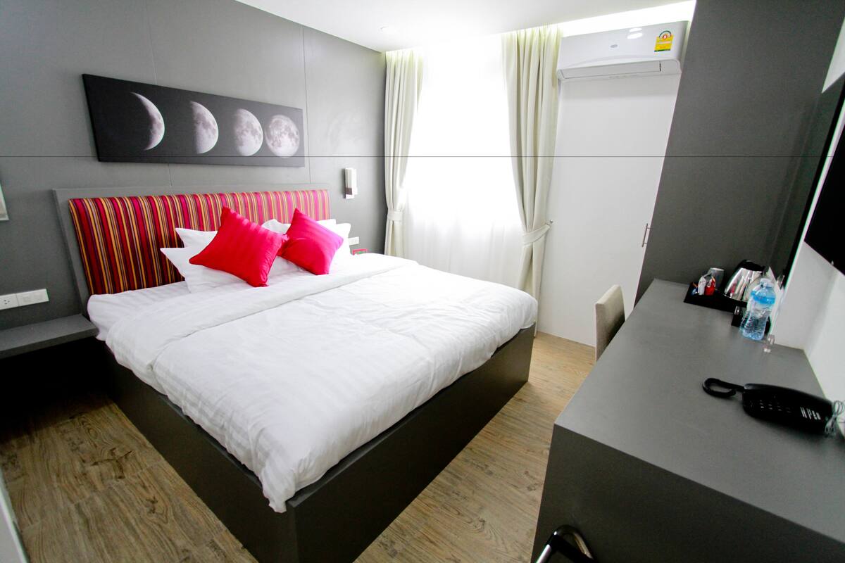 A hotel room with a bed, a desk, a phone, and a wall with a moon phases artwork.